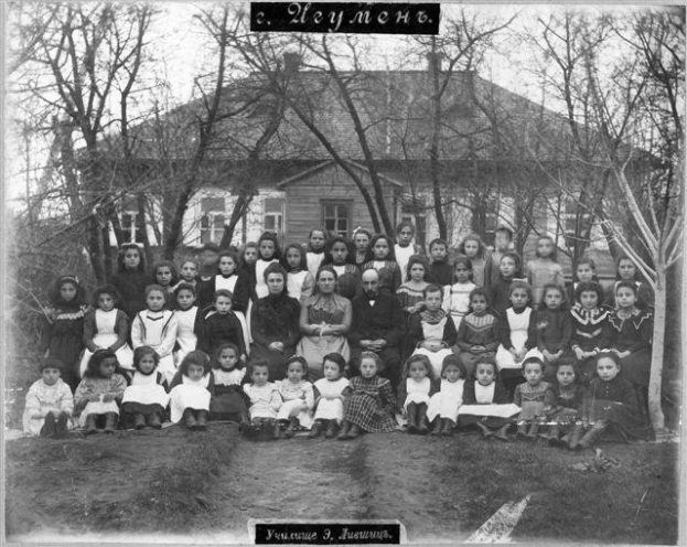 Schwarz-weiß-Foto von Kindern, die vor einem Fensterbau posieren, umgeben von Bäumen und einem klaren Himmel, mit Text unten, der 'Jugoslawien, die erste Schule der Welt' liest.