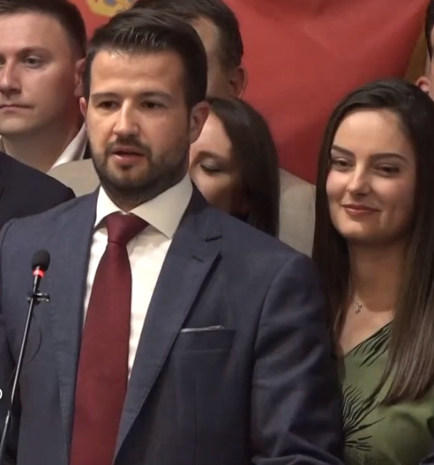 Ein Mann im Anzug spricht an einem Rednerpult mit einem Mikrofon zu einer Menge hinter einem Banner, wahrscheinlich Kommentiert er ein Regierungsverbot der sozialen Medien.