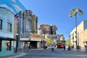 Lebendige StraßenSzene im Universal Studios Hollywood mit Passanten, einem Fahrzeug auf der Straße und umliegenden städtischen Elementen wie Bäumen, Polen und Schildern unter einem sichtbaren Himmel.