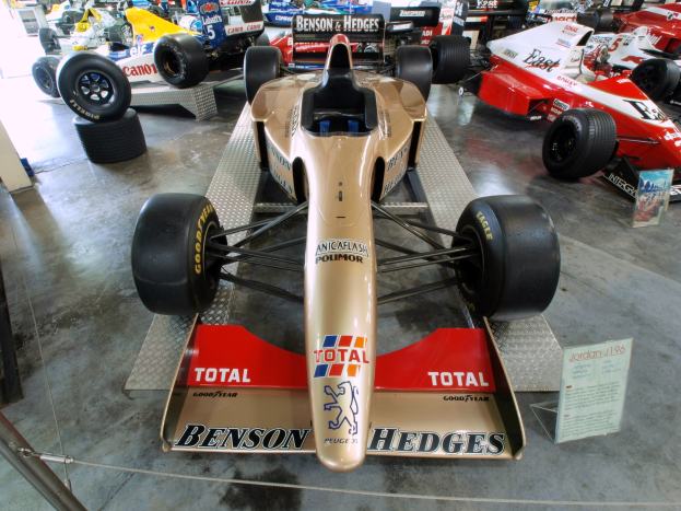 Rennwagen im Museum hinter einem Metallzaun ausgestellt, mit informativem Text und Besuchern im Hintergrund.