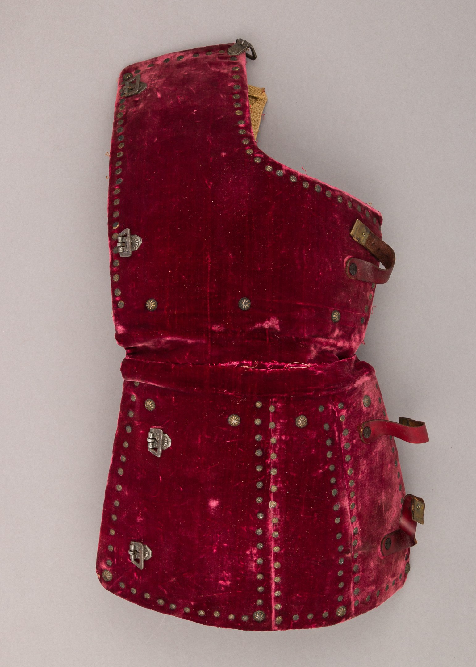 Ein rotes Samtkorsett mit goldenen, mit Strasssteinen besetzten Trägern und silbernen Schnallen auf einer weißen Oberfläche.
