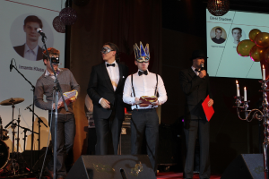 Vier Personen auf einer Bühne, wobei die Person rechts in ein Mikrofon spricht.