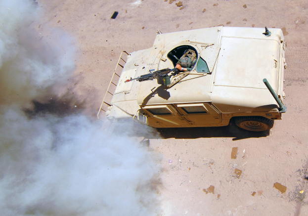 Panzerfahrzeug fährt eine Schotterstraße entlang mit Rauch, der aus ihm aufsteigt und einer Person, die im Inneren sichtbar ist.