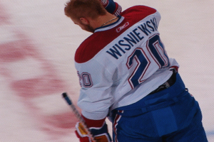 Ein Eishockeyspieler in einem "Wisniewski"-Trikot steht auf dem Eis und hölt einen Hockeyschläger, mit einem konzentrierten und entschlossenen Gesichtsausdruck.