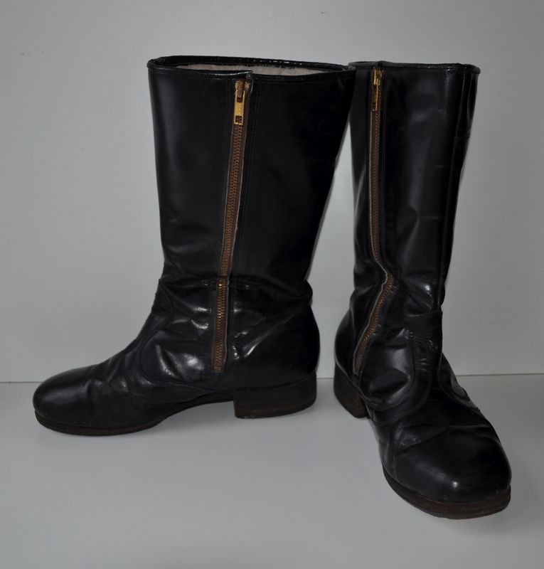 Schwarze Lederstiefel mit silbernen Reißverschlüssen auf einer weißen Oberfläche, mit einem glänzenden Finish.