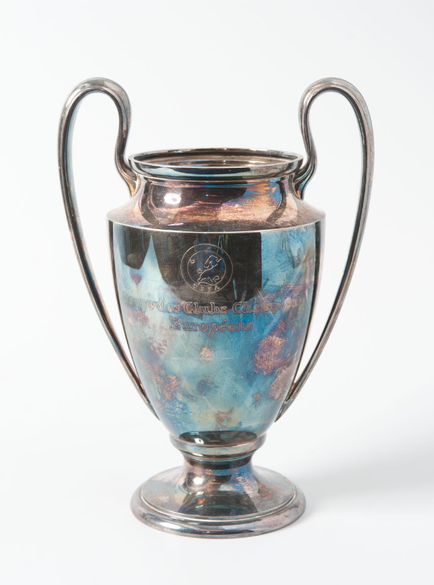 UEFA Champions League-Trophäe, ein stählerner Pokal mit zwei Griffen und einem blauen und silbernen Farbschema, beschriftet mit "UEFA Champions League" vor einem weißen Hintergrund.
