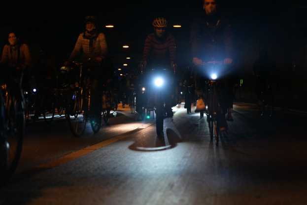 Eine Gruppe von Menschen, die nachts mit Fahrrädern eine Stadtstraße entlangfährt, alle tragen Helme.