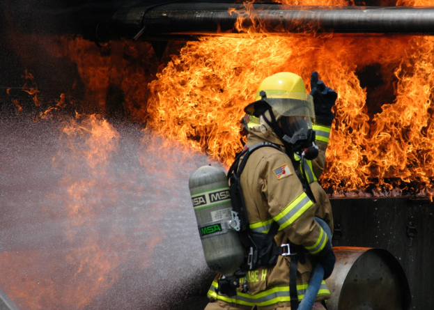 Feuerwehrmann in Schutzausrüstung sprüht Wasser auf ein brennendes Rohr.